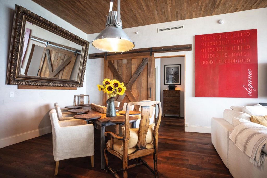 The living/dining area includes a custom table made by Holland, barn doors, a Restoration Hardware lighting fixture, and painting by Holland. Photo by Benjamin Rusnak